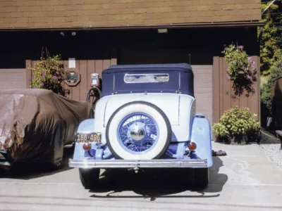 Remastered photo of a blue 1930s classic convertible rear view outside Corvette Connection, showing the rear-mounted spare tire, chrome bumper, and restored vintage styling.