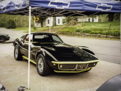 Remastered photo of a black 1968 Chevrolet Corvette convertible front angle under a canopy, showing the chrome bumper, long hood, and restored black exterior finish.