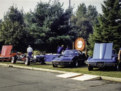 Remastered photo of a Corvette Connection car show display with blue and black classic Chevrolet Corvette convertibles and the round shop sign in the background.