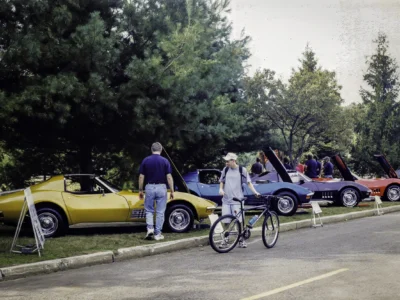 Remastered photo of a Corvette Connection car show display with yellow, blue, and black classic Chevrolet Corvette convertibles lined up with hoods open.