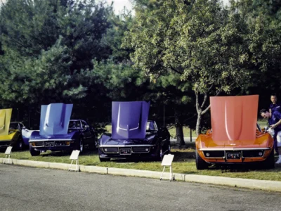 Remastered photo of multiple classic Chevrolet Corvette convertibles displayed at a local car show by Corvette Connection in Bolton, Connecticut, showing blue, black, and red Corvettes lined up with hoods open.