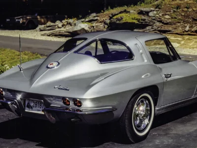 Remastered photo of a silver 1963 Chevrolet Corvette split-window coupe rear angle, showing the iconic split rear window, round taillights, and restored silver paint.